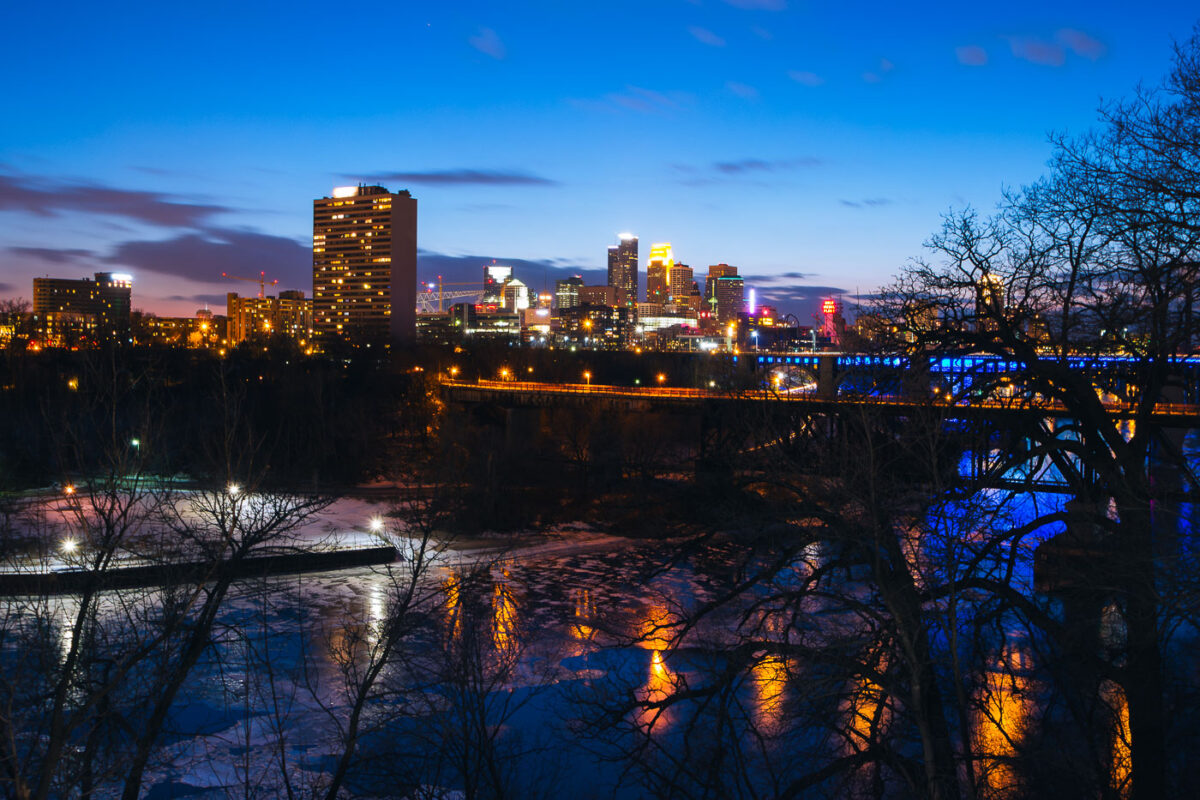 Downtown Minneapolis behind the Mississippi River during blue hour.