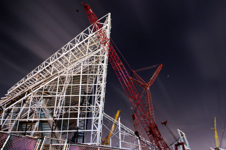 Construction of U.S. Bank Stadium’s Steel Frame, Minneapolis, 3 U.S. Bank Stadium, home of the Minnesota Vikings, began construction in December 2013 on the site of the former Hubert H. Humphrey Metrodome in downtown Minneapolis. The stadium’s steel skeleton, seen here during its mid-construction phase, showcases the dramatic angular geometry that defines its final form — a nod to both Nordic shipbuilding and Minnesota’s icy winter landscapes.
The project, designed by HKS Architects and constructed by Mortenson, features over 19,000 tons of structural steel and spans 1.75 million square feet. Its transparent ETFE roof panels and vast steel trusses were among the most complex structural assemblies ever attempted in a U.S. stadium build.
Completed in 2016, the $1.1 billion stadium remains one of the most technically ambitious indoor venues in North America, notable for its fixed-roof design, massive glass curtain walls, and precision-engineered support cranes like the red lattice boom seen here — used to hoist the roof trusses into place during overnight construction sessions.