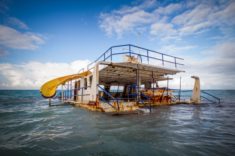 Abandoned Ferry Boat Off Coast of Punta Cana, Dominican Republic 1 This abandoned ferry boat, once likely a mode of transport or perhaps a floating attraction, now rests partially submerged off the coast of Punta Cana in the Dominican Republic. Its rusted hull and decaying structure speak to a forgotten purpose and the relentless passage of time. The presence of a yellow water slide suggests it may have served as a unique excursion vessel or a stationary entertainment platform before its abandonment. The vessel's current state serves as a stark reminder of the transient nature of human endeavors against the backdrop of the Caribbean Sea.