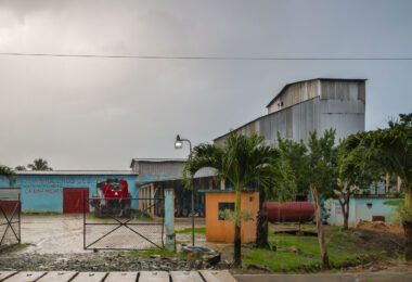 A small agricultural processing facility belonging to a local rice growers’ association in the rural district of La Gina, near Miches in eastern Dominican Republic. Buildings like this serve as cooperative hubs where farmers mill, store, and distribute rice harvested from nearby valleys and foothills. The corrugated steel structures, machinery shelters, and entry kiosk reflect a modest but functional rural agro-industrial operation supporting community-based farming. Rice cultivation has been an important part of the Dominican countryside economy for decades, particularly in the El Seibo and Hato Mayor provinces where smallholder producers rely on local cooperatives for processing and market access.