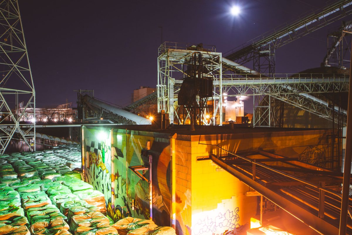 Upper Harbor Terminal barge facility on the Mississippi River in Minneapolis at night, with stacked bulk freight and industrial loading equipment illuminated.