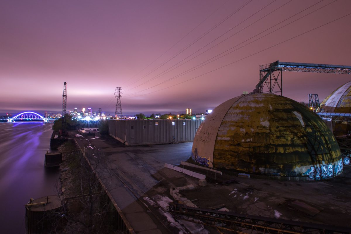 Abandoned barge terminal on the Mississippi River in Minneapolis at dusk, with industrial domes and loading equipment visible.