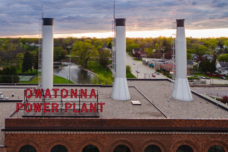 Owatonna Power Plant Neon Sign at Dusk 1 The Owatonna Power Plant in Owatonna, Minnesota, is illuminated by a neon sign at dusk. The brick building features three smokestacks and has historical significance for local industrial history.