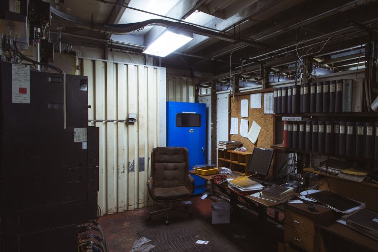 Cluttered industrial office space inside a steel mill with a blue door, desk, and filing cabinets.