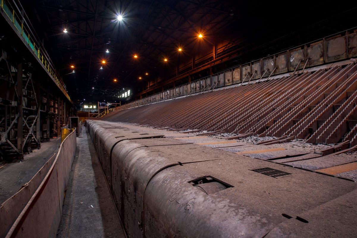 Abandoned steel mill floor at ArcelorMittal in East Chicago with industrial pipes, seating, and overhead lighting.