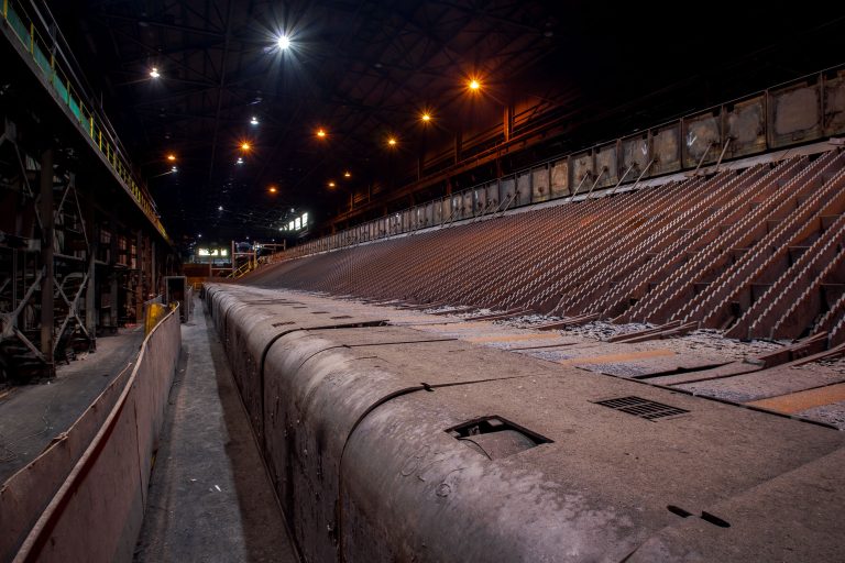 Cooling Beds at ArcelorMittal's East Chicago Works 3 Abandoned steel mill floor at ArcelorMittal in East Chicago with industrial pipes, seating, and overhead lighting.