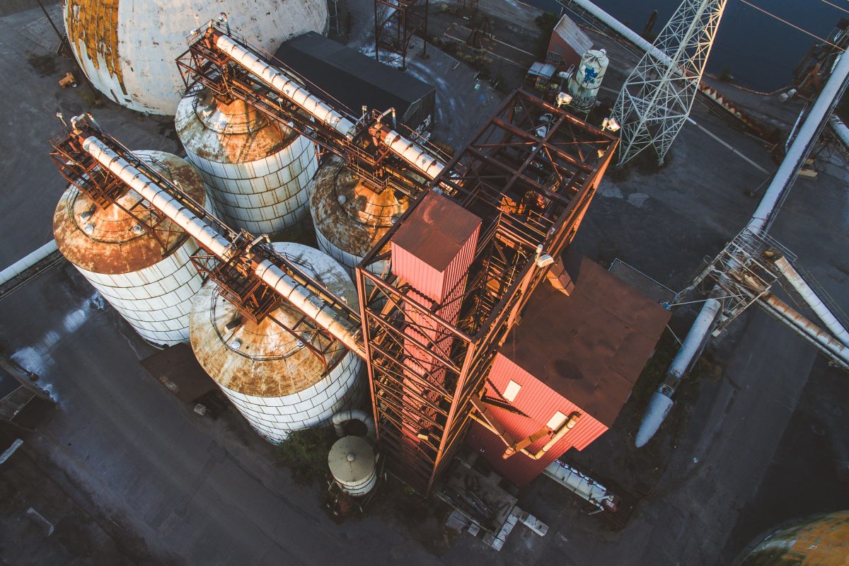 Aerial view of rusted storage domes and orange loading equipment at Upper Harbor Terminal, a defunct barge facility on the Mississippi River in Minneapolis.