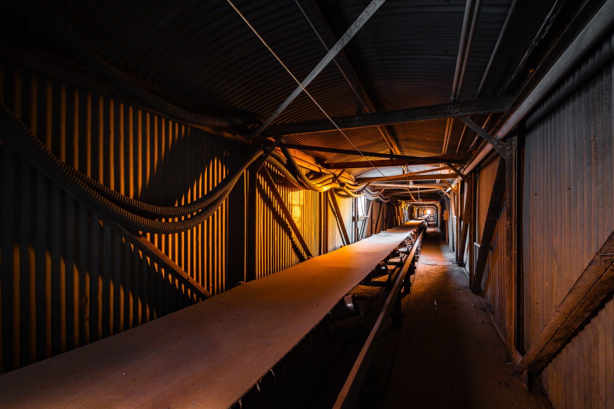 Interior of Electric Steel grain elevator in Minneapolis showing a long conveyor belt beneath industrial metal framework and corrugated walls.