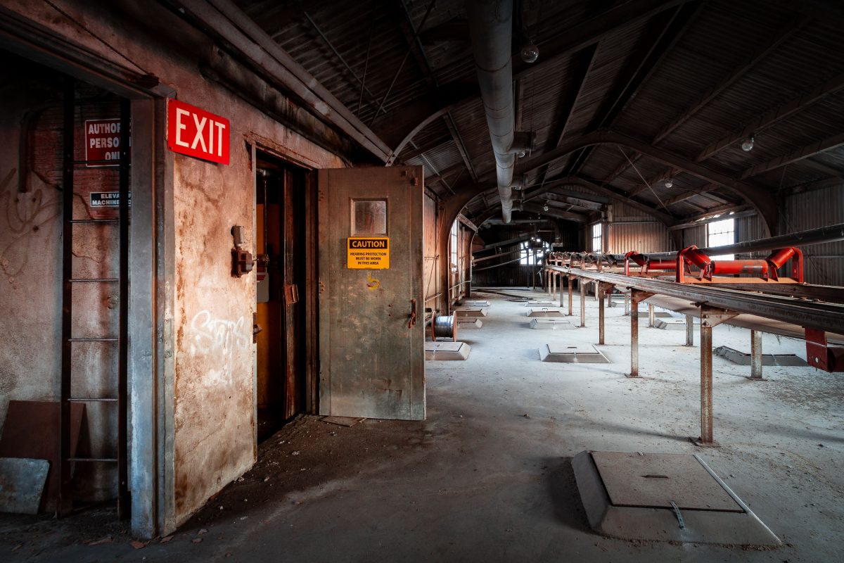 Abandoned Electric Steel grain elevator interior in Minneapolis with rusted machinery, conveyor systems, and red exit sign.