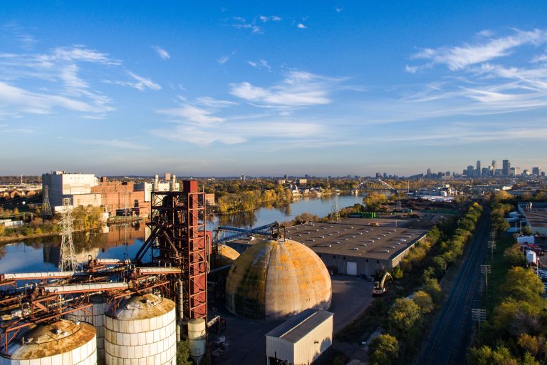 Upper Harbor Terminal with the Minneapolis Skyline Beyond 1 Upper Harbor Terminal, a former barge facility on the Mississippi River in north Minneapolis, sits idle with storage tanks and industrial structures visible.