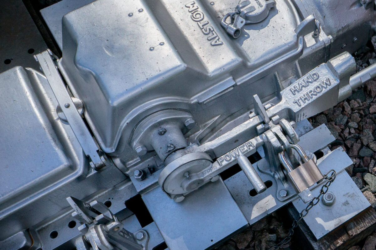 A close-up of an Alstom railway switch machine, showing the locked levers for power and hand-throw operation, used to control train track switches.