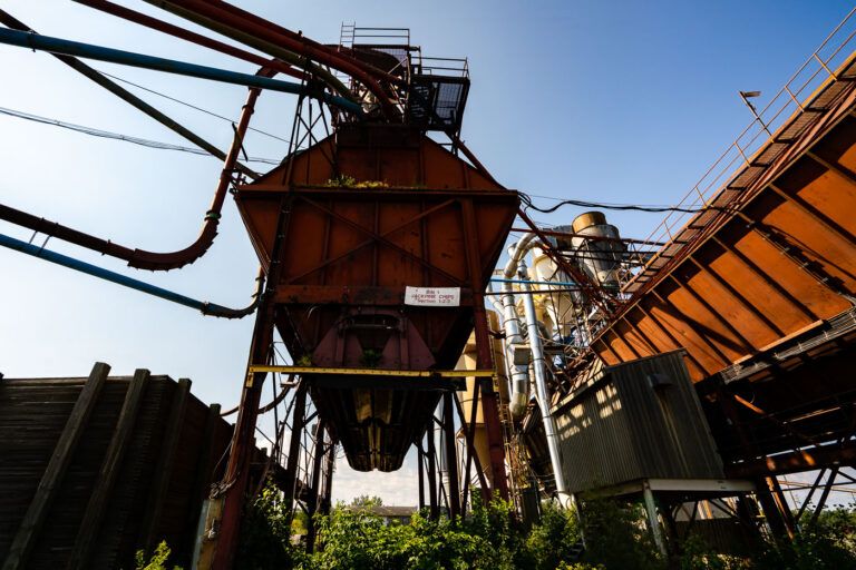 Conveyor Systems at the Former Great West Lumber Sawmill, Thunde 3 The rusting conveyor systems and storage bins of the former Great West Lumber Sawmill stand as remnants of Thunder Bay’s once-thriving forest industry. Established near the Lake Superior waterfront in the early 20th century, the mill was part of a vast network that processed and shipped lumber across North America. Its maze of steel ducts and conveyors once carried sawdust, chips, and milled timber, feeding the region’s economic boom. Today, the overgrown machinery reflects a post-industrial landscape—silent evidence of a city that helped fuel Canada’s forestry trade for generations.