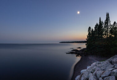 Evening settles over the North Shore as the moon rises above Lake Superior, seen from Silver Creek Township, Minnesota. The calm waters reflect the fading light of dusk along a rugged basalt shoreline shaped by ancient lava flows nearly a billion years old. This stretch of coast, north of Two Harbors, remains one of the most geologically significant and least developed sections of Minnesota’s Superior shoreline—where forests of spruce and pine meet one of the world’s largest freshwater lakes under an endless sky.