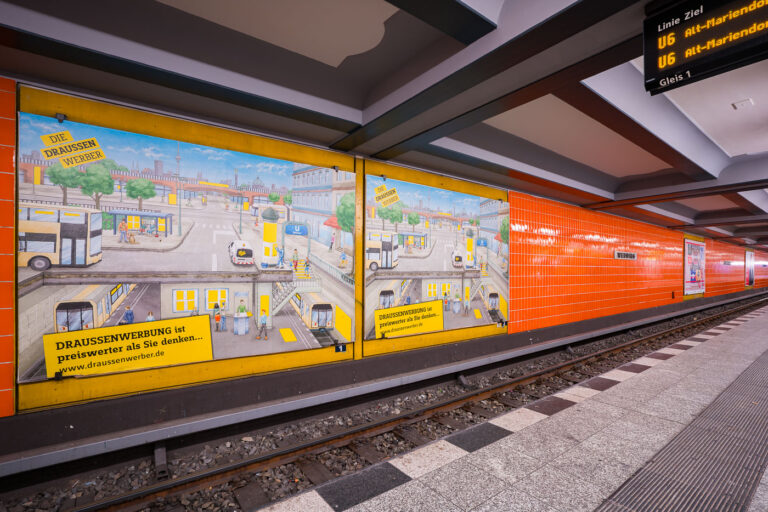 Berlin Wedding train station 3 Wittenbergplatz station on Berlin’s U2 line features a distinctive orange-tiled design characteristic of the city’s postwar modernization of U-Bahn interiors. The platform level seen here includes advertising panels with hand-illustrated city scenes, part of a campaign promoting outdoor advertising (“Draussenwerbung”) by Wall GmbH, a longtime transit advertising company in Berlin.Opened in 1902 as part of the city’s first underground railway, Wittenbergplatz is one of Berlin’s oldest stations and a key junction serving the U1, U2, and U3 lines. The orange tiles were installed during mid-20th-century refurbishments to brighten the subterranean space, contrasting with the original Jugendstil architecture preserved at the main hall above. The modern signage displays U6 connections, while the station’s layout—with three island platforms—continues to serve one of the busiest interchange points in Berlin’s U-Bahn network.