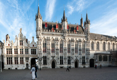 Bruges City Hall (Stadhuis van Brugge), completed in 1421, is one of the oldest and most ornate Gothic town halls in the Low Countries. Located on Burg Square in the heart of Bruges, Belgium, the structure features a richly detailed facade with vertical pinnacles, traceried windows, and over fifty sculpted figures representing biblical and historical figures important to the city’s heritage. The red dormer windows punctuating the steep slate roof are typical of Flemish civic architecture from the period. To the left, the adjoining Renaissance-style Oude Civiele Griffie (Old Civil Registry), built in 1537, complements the Gothic hall with gilded stonework and classical ornamentation. Together, the buildings form a symbolic center of Bruges’ civic identity and remain a key stop for visitors exploring this UNESCO World Heritage city.