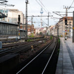 Eastward Curve at Berlin Friedrichstraße 3 Tracks curve eastward from Berlin Friedrichstraße station, one of the city’s busiest S-Bahn and regional rail interchanges. The elevated viaduct carries multiple lines, including the S3, S5, S7, and S9, which link central Berlin with its outer districts and neighboring cities. The view looks toward Alexanderplatz, with the Fernsehturm television tower visible in the distance — a defining landmark of the former East Berlin skyline.
Friedrichstraße station opened in 1882 and served as a symbolic and logistical border crossing during the Cold War, when it connected both East and West Berlin rail networks. Today, the station remains a major transit hub, handling thousands of passengers daily and sitting at the junction of the north–south and east–west S-Bahn corridors. The surrounding area has since been redeveloped with modern offices, hotels, and shops while retaining its role as one of Berlin’s central transport arteries.