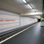 Kurt-Schumacher-Platz station serves Berlin’s U6 U-Bahn line in the Reinickendorf district, located in the city’s northwest. Opened on May 3, 1956, the station was part of the first postwar U-Bahn expansion and named after German statesman Kurt Schumacher, a key figure in rebuilding the Social Democratic Party after World War II.

The station features light-colored wall tiles with horizontal gray stripes and minimalist red lettering, reflecting mid-1950s West Berlin design. It includes a central island platform and two tracks, serving as an important stop between Afrikanische Straße and Scharnweberstraße. Above ground, the station connects to several bus routes and lies near the approach to the U6 tunnel under the former Tegel Airport area. Today, it remains a key link for northern Berlin commuters traveling toward the city center.