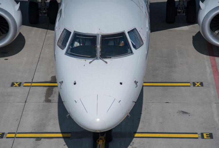 Airbus Cockpit Preflight Checks 2 An Airbus narrow-body jet prepares for departure on a bright afternoon, its cockpit crew performing preflight procedures before pushback. The aircraft’s clean nose profile reveals pitot tubes, static ports, and the angular geometry typical of the A320 family. Yellow taxiway markings and the tow bar connection below hint at the precision choreography of ground operations—where every motion, from refueling to final clearance, is timed to the minute. Captured from above, the composition highlights the symmetry and order that define modern commercial aviation.