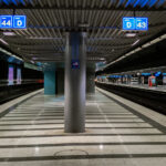 An underground train platform at Zürich Airport station, with tracks 43 and 44 visible. The station features striped tile flooring, overhead signage, and modern lighting. Few passengers are present, and escalators can be seen in the background leading to the upper levels.