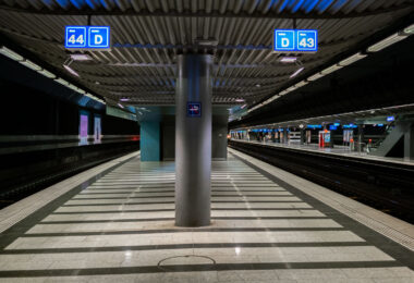 An underground train platform at Zürich Airport station, with tracks 43 and 44 visible. The station features striped tile flooring, overhead signage, and modern lighting. Few passengers are present, and escalators can be seen in the background leading to the upper levels.