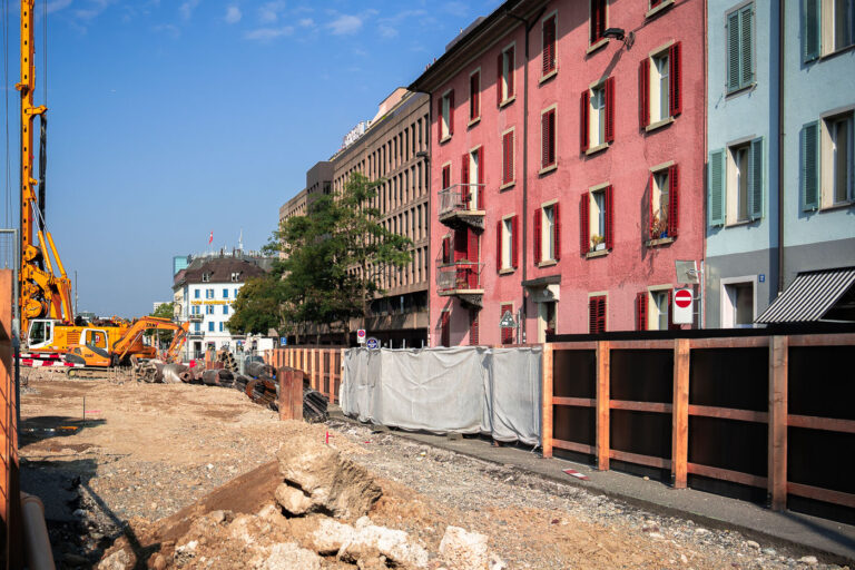 Zurich Construction Site with Residential and Office Buildings 1 Construction is ongoing in Zurich, Switzerland, on a site that will house residential and office buildings. The project involves heavy machinery, including a large drilling rig, and materials such as steel rebar and concrete. Adjacent to the active construction zone, existing colorful residential buildings stand alongside modern office structures, illustrating the city's continuous development. This development reflects Zurich's status as a major global financial center and its ongoing efforts to expand its urban infrastructure and housing capacity.