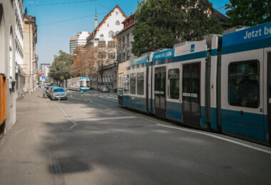 Two blue-and-white Zürich trams move through a broad, tree-lined avenue near the city center, a familiar sight in the Swiss metropolis where public transport defines the pace of daily life. Operated by VBZ, the Zürich tram network dates back to the 1880s and remains one of Europe’s most efficient urban systems, linking every corner of the city with clockwork precision. The clean lines of the vehicles, the restrained architecture, and the soft autumn light together reflect the city’s balance of historic character and modern functionality — a seamless integration of movement, order, and urban calm.