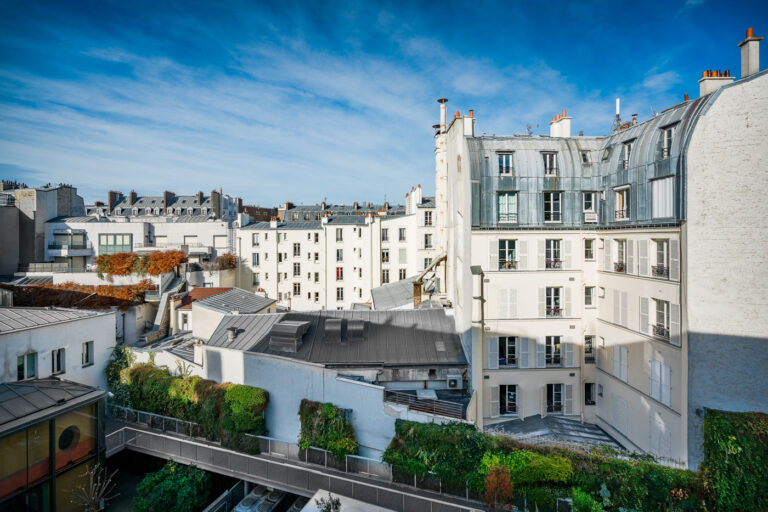 Paris 9th Arrondissement Apartment Buildings, Autumn Sky 3 Apartment buildings in Paris's 9th arrondissement showcase Haussmannian architectural influences, characterized by their white facades, mansard roofs, and dormer windows, typical of late 19th-century urban development. These structures were designed to create a uniform and elegant streetscape, a hallmark of Baron Haussmann's renovation of Paris. The presence of a modern glass extension and vertical gardens indicates contemporary adaptations within these historic residential blocks, reflecting the ongoing use and modernization of Parisian housing.