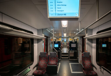 An early morning S-Bahn train heads toward Zürich Hauptbahnhof, Switzerland’s busiest railway hub. The interior, illuminated by soft fluorescent lighting and digital displays, reflects the precision and cleanliness that define Swiss rail travel. With clearly marked stops and ergonomic seating, the S-Bahn system connects Zürich’s suburbs to the city center with remarkable efficiency and punctuality.

The Zürich S-Bahn network began operation in 1990 as one of Europe’s first regional rail systems to integrate multiple operators under a unified timetable. Zürich HB serves as its central interchange, handling over 400,000 passengers daily and linking regional, national, and international routes. This modernization transformed local commuting and reinforced Switzerland’s reputation for world-class rail infrastructure.