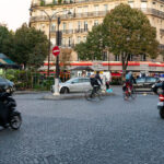 Evening commuters navigate the cobblestone intersection at Place de l’Alma, a busy roundabout near the Seine that connects several major Parisian avenues. Cyclists, scooters, and cars intermingle beneath the façades of Haussmann-era buildings, a familiar rhythm in the city’s daily life. The area blends elegance and intensity—its limestone balconies and cafés standing in contrast to the constant motion of urban transit.

Completed in the mid-19th century, Place de l’Alma became a symbolic gateway between the Right Bank and the Left, linking the fashionable avenues of the 8th and 16th arrondissements. The nearby Pont de l’Alma, inaugurated in 1856 by Napoleon III, was once guarded by four statues of French soldiers—only one, the Zouave, remains today, still serving as an informal flood gauge for the rising Seine.