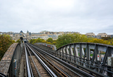 Paris Metro Line 6 crosses the Seine on the Pont de Bir-Hakeim, a two-level bridge completed in 1905 that combines roadway, pedestrian walkway, and elevated railway. The steel viaduct, designed to support one of the city’s earliest elevated metro lines, features riveted beams typical of early 20th-century engineering. In the distance is the Passy district in the 16th arrondissement, known for its Haussmann-era architecture and ornate façades. This elevated section of Line 6 was intentionally built above ground to provide air circulation for the early steam-powered trains, making it one of the few Paris metro routes that offer open views of the city’s urban landscape.