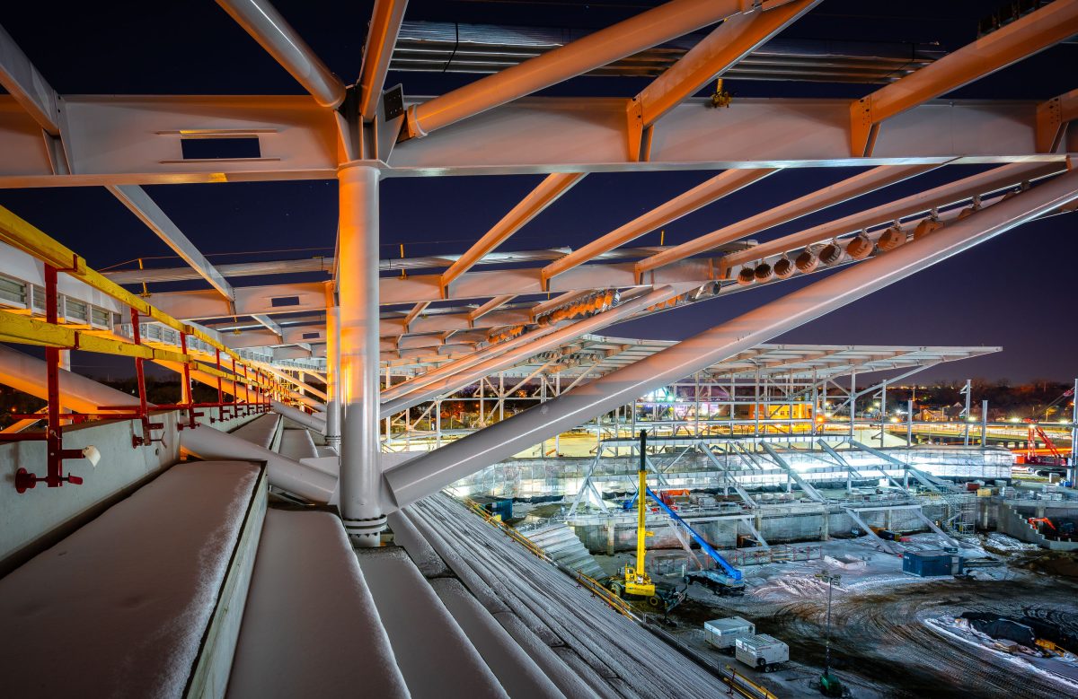 Nighttime construction of Allianz Field stadium in St. Paul showing illuminated steel beams and concrete foundation work.