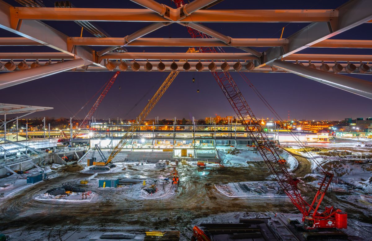 Nighttime construction site of Allianz Field stadium in St. Paul with illuminated steel framework and red cranes.