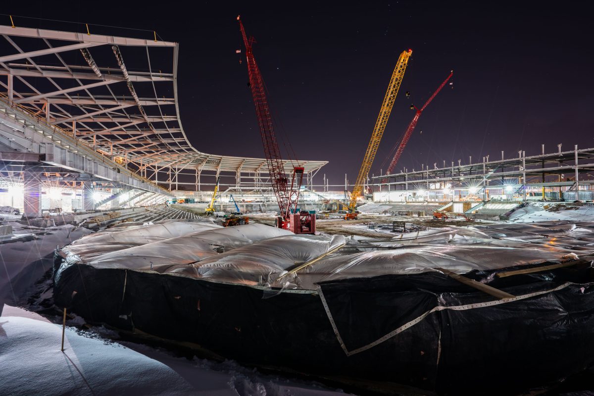 Allianz Field stadium under construction at night in St. Paul with illuminated cranes and steel structural framework.