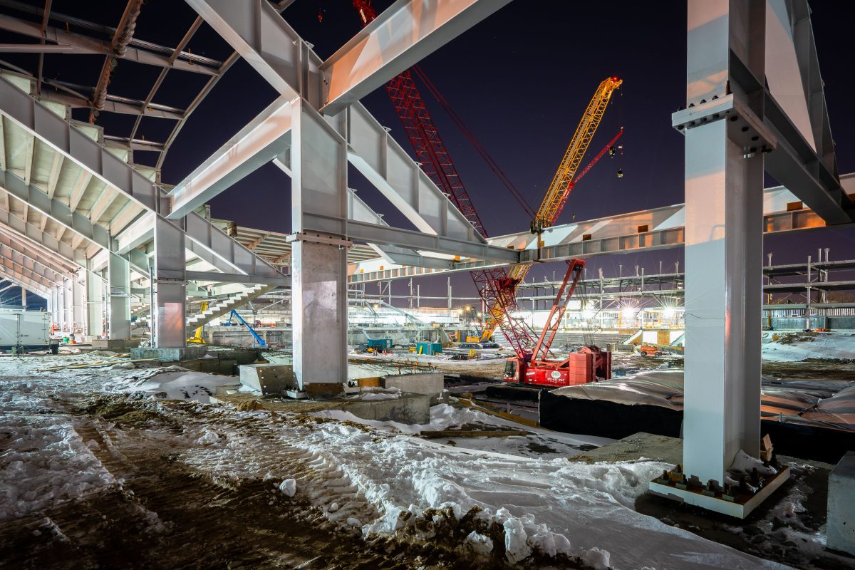 Nighttime construction of Allianz Field stadium in St. Paul with illuminated cranes and concrete structural supports.