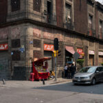 Corner of Calle República de Uruguay and Calle 5 de Febrero 2 A busy corner in Mexico City’s Centro Histórico where Calle República de Uruguay meets Calle 5 de Febrero. The block’s centuries-old volcanic stone buildings, typical of the colonial period, now house small shops and street vendors that reflect the area’s dense commercial activity. The facade’s weathered cantera stone and red tezontle give the structure its distinctive character, common in pre-19th century civic architecture throughout the historic core.
