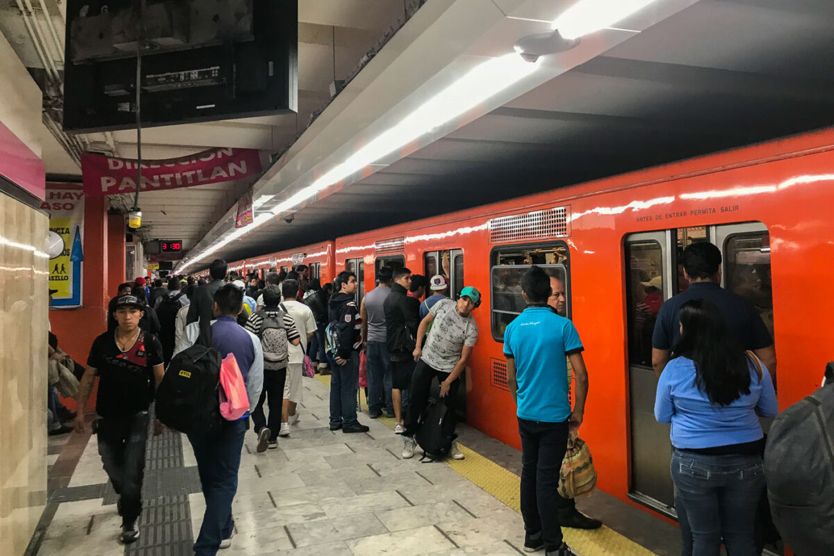 Passengers wait on the platform at Pantitlan Station, a major transfer point for Mexico City Metro Lines 1, 5, 9, and A. An orange train is stopped at the platform.