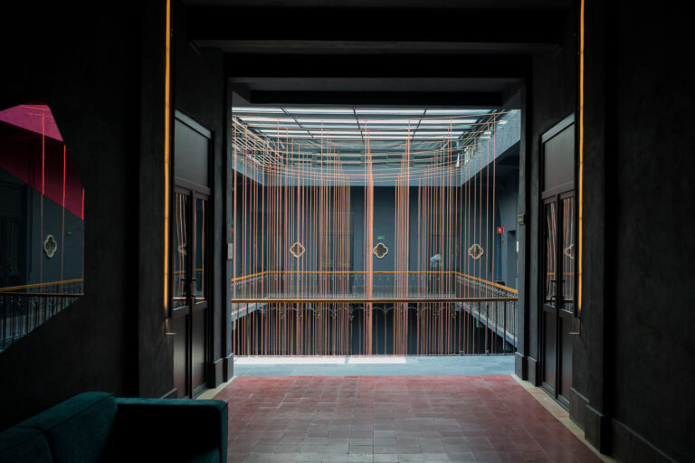 Modern Atrium Design in Historic Mexico City Hotel 1 A contemporary atrium design inside a boutique hotel in central Mexico City, featuring suspended copper lines, geometric window accents, and minimalist lighting that contrasts with the historic colonial structure it occupies. The building, located near the heart of the Centro Histórico district, reflects the city’s growing trend of adaptive reuse—where heritage buildings are renovated to blend preserved masonry and ironwork with sleek, modern interiors.