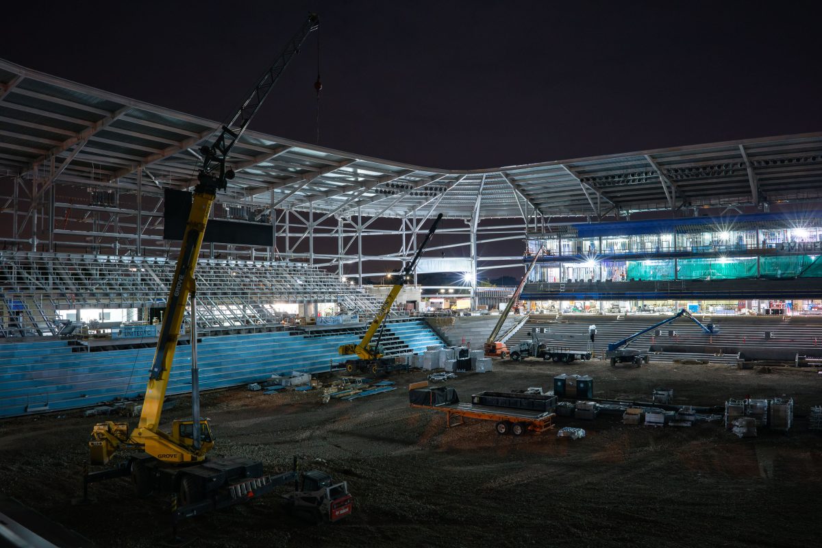 Yellow mobile crane operates inside Allianz Field stadium under construction at night in St. Paul.