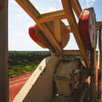 Viewed from behind the machinery, the pumpjack overlooks a sweeping stretch of North Dakota badlands. Its rusted gears and faded paint contrast sharply with the vivid red earth and green hills—a scene that captures both the rugged beauty and industrial imprint of the oil fields.