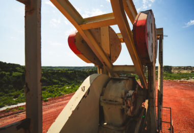Viewed from behind the machinery, the pumpjack overlooks a sweeping stretch of North Dakota badlands. Its rusted gears and faded paint contrast sharply with the vivid red earth and green hills—a scene that captures both the rugged beauty and industrial imprint of the oil fields.