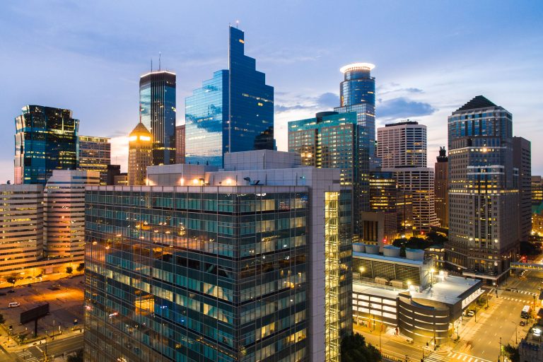 Downtown Minneapolis skyline at dusk with illuminated office towers and streets below.