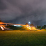 Winter Park in Eden Prairie, Minnesota, served as the long-time headquarters and training facility of the Minnesota Vikings from its opening in 1981 until the team’s move to the Twin Cities Orthopedics Performance Center in 2018. The low-profile, bunker-like structure was designed to blend into the grassy landscape, housing offices, locker rooms, weight facilities, and the iconic indoor practice field under its distinctive inflated roof. The illuminated building and outdoor practice fields seen here reflect its primary role as a working athletic campus rather than a public venue. Even after operations shifted, the site remained symbolically tied to the team’s formative decades, including the Herschel Walker trade years, early indoor training innovations, and the development of multiple Pro Bowl players.