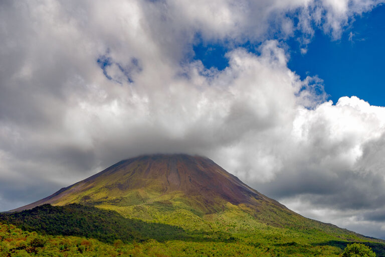Arenal Volcano, Costa Rica 3 Arenal Volcano in Costa Rica is partially obscured by clouds, with lush green vegetation in the foreground.