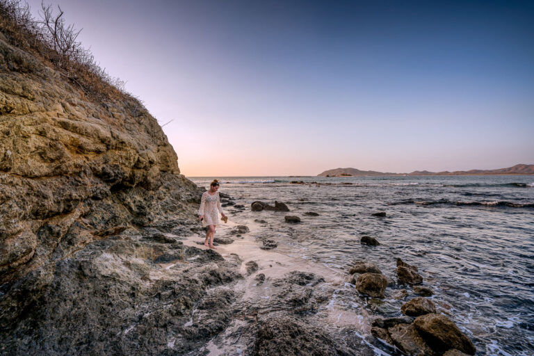 Punta San Francisco Beach, Costa Rica 4 A woman walks on the rocky shore of Punta San Francisco Beach, Costa Rica, at dusk. The Pacific Ocean waves meet the sand and rocky cliffs.