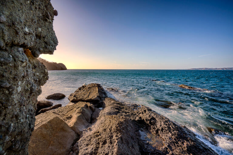Sunset on the shore in Costa Rica 1 The sun sets over Jabo Bay on the Pacific coast of Costa Rica. This bay is part of the Nicoya Peninsula, a region known for its diverse ecosystems and popular beaches. The rugged, rocky shoreline in the foreground is characteristic of many coastal areas in this part of Central America. Jabo Bay is a natural harbor that has likely been used by local communities for centuries for fishing and as a point of access to the sea.