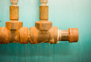 Rust-streaked industrial valves, stamped with “MOA Forged” and “BONNEY,” mounted against a teal wall, showing the wear of age and use.