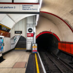 The southbound Bakerloo line platform at Charing Cross Underground Station in central London, showing the distinctive narrow tube tunnel built in the early 1900s. The red-edged lining around the tunnel mouth and the tiled passageway reflect classic London Transport design standards. Opened in 1906, the Bakerloo line was one of the early deep-level “tube” lines, and this station once served as its southern terminus before extensions carried it to Elephant & Castle. The signage and steep staircases illustrate the compact engineering that defined London’s early subterranean railways.