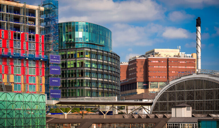 Canal Walk Apartments Construction, London 3 Construction of Canal Walk Apartments in London, featuring modern glass and red-clad buildings alongside older industrial architecture and a spiral chimney.
