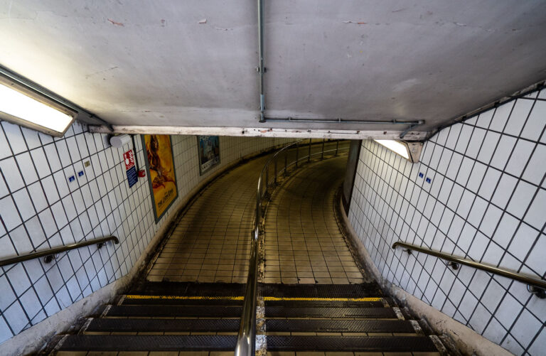 Underground Passageway at Charing Cross Station 4 Descending into the tiled corridors of Charing Cross Station, this curved passageway reflects the classic utilitarian design of the London Underground’s mid-20th-century refurbishments. The white-tiled walls, stainless-steel handrails, and fluorescent lighting form a distinctly familiar aesthetic across the network, guiding travelers toward the Northern and Bakerloo lines. Once part of the original terminus for trains entering central London, Charing Cross remains a vital interchange linking rail and Tube services near Trafalgar Square—its passages echoing the constant rhythm of London commuters.
