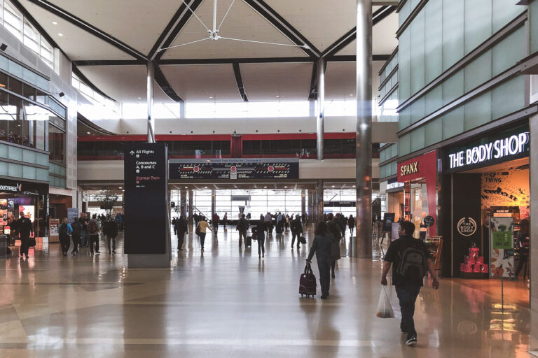 McNamara Terminal Concourse A – Detroit Metro Airport 1 Inside Concourse A of Detroit Metropolitan Wayne County Airport (DTW), travelers move through the main corridor of the McNamara Terminal, a hub designed around Delta Air Lines operations. The terminal’s mile-long concourse, opened in 2002, features the elevated red ExpressTram gliding silently above the concourse, linking distant gates in under two minutes. Glass storefronts, high ceilings, and modern lighting reflect DTW’s role as one of the most efficient and architecturally forward airports in North America. The photo captures the rhythm of early-morning movement — passengers, luggage, and signage converging under the massive steel-truss ceiling.